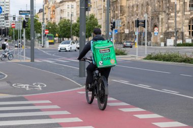 Poznan, Polonya - 10 Ağustos 2025: Uber, yemek teslimatları için yeşil markalı bir termal çanta taşıyarak, bir şehir caddesinde bisiklet kuryesi yiyor