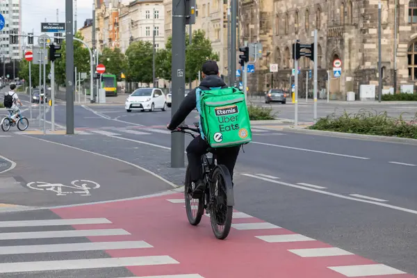 Poznan, Polonya - 10 Ağustos 2025: Uber, yemek teslimatları için yeşil markalı bir termal çanta taşıyarak, bir şehir caddesinde bisiklet kuryesi yiyor