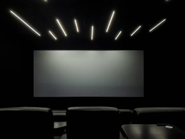 Konforlu oturma ve düzgün tavan lambaları ile tamamlanmış, karanlık, modern bir ev sinemasında içerik bekleyen boş projeksiyon ekranı, medya olayları veya özel gösterim için ideal