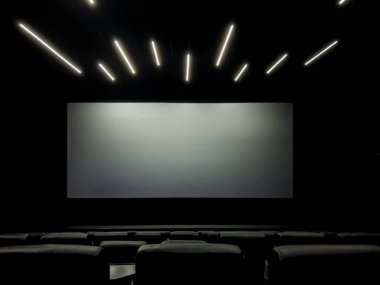 Çağdaş, karanlık bir sinema salonunun içine bakın, tavanda şık bir doğrusal aydınlatma, büyük boş bir projektör ekranı, ve seyirci için parlak koyu renkli koltuklar
