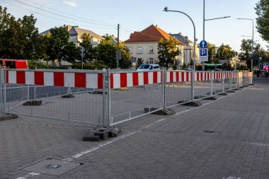 Şehir sokaklarında bir inşaat alanını delen yansıtıcı kırmızı ve beyaz panellerle uzun sıra metal güvenlik bariyerleri, halkın güvenliğini sağlıyor.