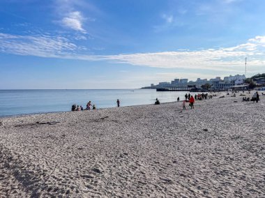 Değişik insan gruplarıyla dolu canlı kumlu bir sahilin panoramik görüntüsü berrak bir mavi gökyüzünün altında dinleniyor ve yürüyor, sakin bir yaz tatili havası yakalıyor.