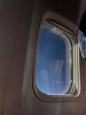 Yüksek irtifa gökyüzüne parlak, açık bir bakış açısıyla bir uçak penceresinin yakın perspektifi, başarılı bir tatili, iş seyahatini veya barışçıl bir yolculuğu temsil eder.