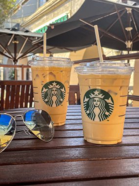 Rhodes, Yunanistan - 23 Eylül 2021: Starbucks 'ta serinletici iki buzlu kahve içeceği ve ahşap bir kafe masasında güneş gözlüğü, açık havada güneşli bir yaz rahatlığının somut örneği.