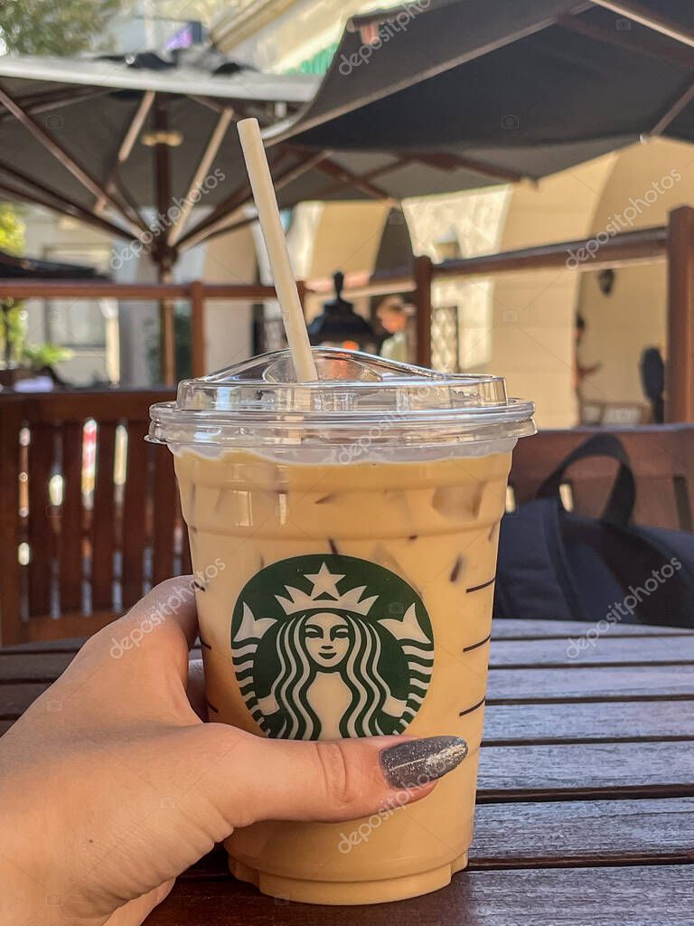 Rhodes, Greece - September 23, 2021: Close-up of a refreshing Starbucks iced coffee, held by a hand with glitter nails, on a wooden table at an outdoor cafe