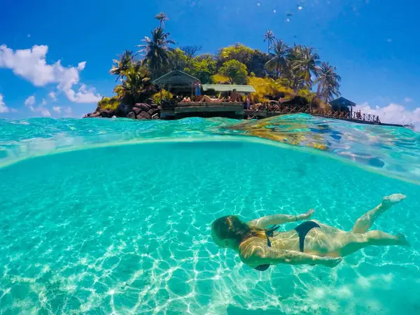 Siyah bikinili bir kadın güneşli bir günde kristal berrak sularla denize dalıyor.