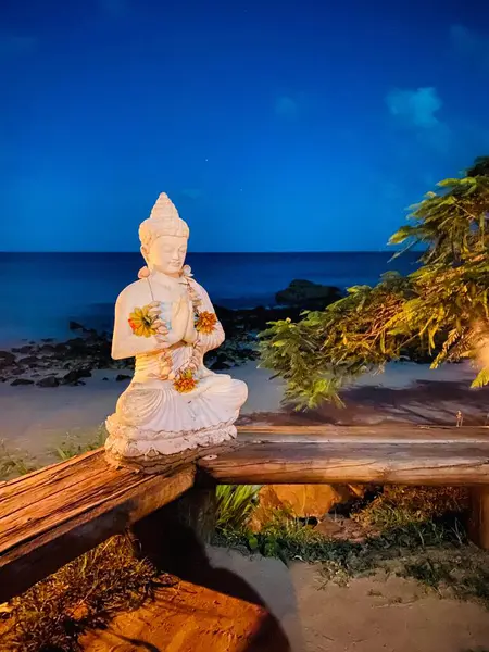 Arkasında okyanus olan ahşap bir güvertede Hawaii kolyesi olan Buda.