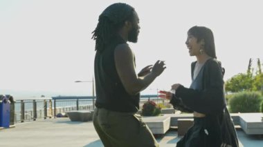 Gün batımında dans eden ve el ele tutuşan mutlu ve etnik çeşitlilikte genç bir çiftin Slow Motion videosu..