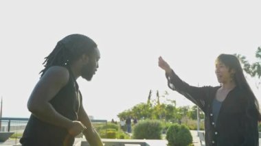 A heartfelt moment unfolds as an African American and Asian couple dance playfully by the water at sunset.