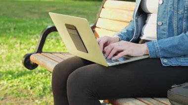 Uzaktan kumandalı bir işçi, ahşap bir banktan yazarken, bir kamu parkında akışını teknoloji ve sükuneti dengeleyerek buluyor..