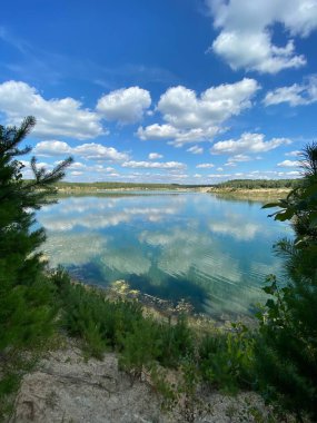 Temiz suyu ve görünür yosunları olan güzel bir göl. Mavi gökyüzünde kabarık bulutlar, yemyeşil bitkiler ve kıyı boyunca yeşillik ile doğal manzara çarpıcıdır..