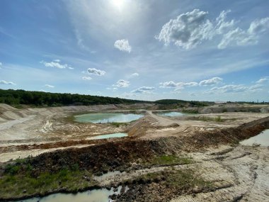 Güneşli bir gökyüzünün altındaki terk edilmiş bir taş ocağının yatay görüntüsü engebeli araziye dağılmış birkaç güzel mavi göl içeriyor..