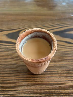 Bir fincan kil çayın yakın plan fotoğrafı. Çay koyu kehribar renginde ve köpüklü bir bluzu var. Kupa ahşap bir masanın üzerinde duruyor..