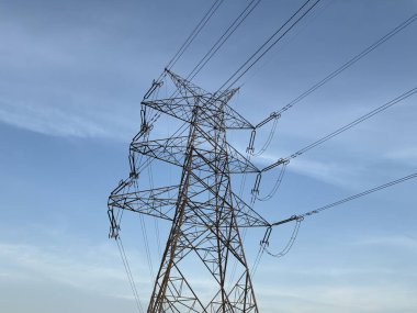 Açık mavi gökyüzüne karşı yüksek voltajlı uzun metal şanzıman kulesi.