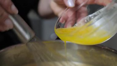 Krep hamuru hazırlanıyor. Aşçı koyu bir kasede yumurta, şeker ve süt karışımı karıştırarak erimiş tereyağı ekler. Metal karıştırıcıyla hamur yoğurmak. Yüksek kalite 4k görüntü