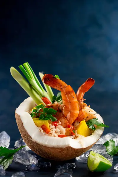 stock image Asian rice dish with tiger prawns, pineapple and lemongrass served in a fresh coconut on a dark background