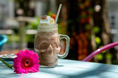 A vibrant milkshake served in a Mexican skull glass, topped with a perfectly toasted marshmallow, set against a bright summer table. This playful and colorful presentation is ideal for beverage and dessert photography themes clipart