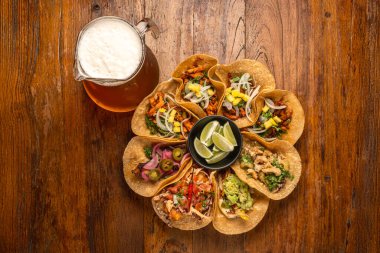 Mısır tortilla ve bira sürahisi ile çeşitli tacoların sade fotoğrafları kırsal arka planda servis ediliyor.