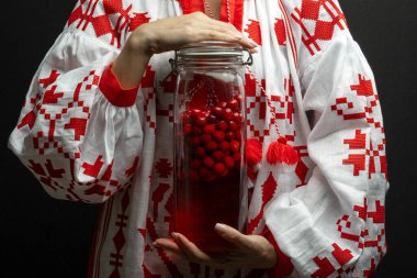 Woman in Ukrainian Traditional Vishivanka dress holding traditional infused cranberries spirit - nalyvka clipart