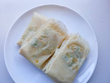 Martabak Telur Kulit Lumpia. Yumurta, et ve yeşil soğan dolgulu çıtır aperatifler. Yeşil biberle yenen favori sokak yemeği. Beyaz tabakta kızarmadan önce.