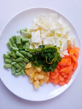 Patates dilimleri, lahana, havuç, yeşil fasulye, tabakta kırmızı soğan sarımsağı ve beyazı izole et. Sağlıklı gıda konsepti. diyet menüsü kavramı