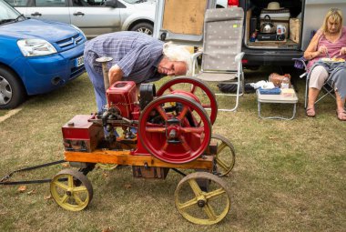 Adamın biri 1915 model Amanco Chore Boy sabit motorlu West Sussex, İngiltere 'deki Wisborough Green Village Fete' e doğru eğildi..