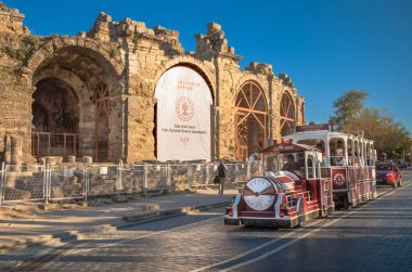 Türkiye 'nin Antalya ilinin Yanındaki antik Roma kentinde bulunan amfitiyatronun kalıntılarından geçen sahte tren veya tramvay turistleri taşıyor. (Türkiye))