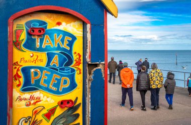 İnsanlar Teignmouth, Devon, İngiltere 'de deniz kenarında eski moda bir dikiz şovu standının önünden geçiyor.