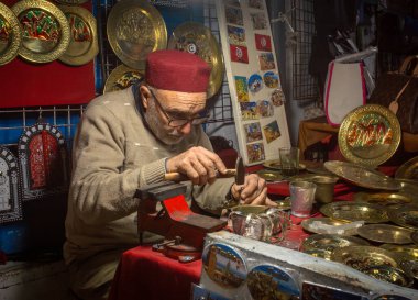 Fes şapkalı bir metal işçisi Tunus 'un Susa kentindeki çarşıdaki turist hediyelik eşya dükkanında çekiç kullanıyor. Medine UNESCO 'nun Dünya Mirası Bölgesi
