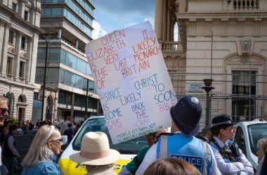 Londra 'da bir polis memuru, 2 Haziran 2022' de Kraliçe 'nin platin yıldönümünü kutlayan kalabalığın arasında duran yalnız bir dini protestocunun plaketine bakıyor..
