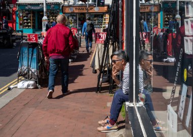 Dükkan sahibi, Brighton, Doğu Sussex, İngiltere 'de bir alışveriş merkezi olan The Lanes' de sigara içerek kapısında oturuyor..