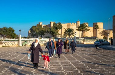 A group of Tunisian women walk near the ancient Islamic fortress the Ribat of Monastir, Monastir, Tunisia clipart