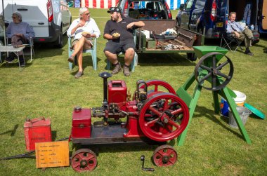 A father and son who are vintage stationary engine enthusiasts sit and show off their 1911 Amanco machine at a village fete in Wisborough Green, West Sussex, UK. clipart