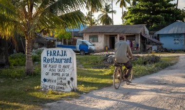 Bir adam, Faraja Restoranı, Jambiani, Zanzibar, Tanzanya için elle boyanmış bir tabelayı geçiyor.