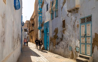 Tunus halkı Tunus 'taki Kairouan antik Medine' deki evlerin önünden geçiyor. Kairouan İslam 'ın dördüncü en kutsal şehridir ve UNESCO' nun Dünya Mirasları Alanıdır..
