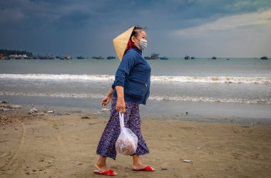 Geleneksel konik şapka takan orta yaşlı Vietnamlı bir kadın My Khe Beach, Danang, Vietnam 'da bir çanta deniz ürünü taşıyor..