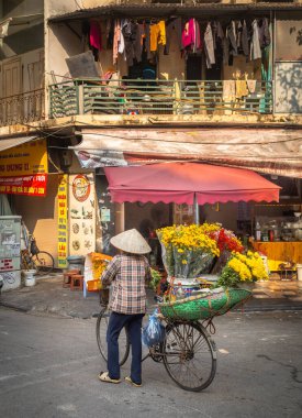 Bir çiçekçi yüklü bisikletini Hanoi, Vietnam 'daki Eski Mahalle' de Cau Go 'da bir restoranın önünden geçirir..