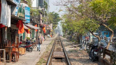 Yüz maskesi takan yaşlı Vietnamlı bir adam ana kuzey-güney demiryolu boyunca yürüyor ahşap mobilya dükkanlarının yanından geçiyor ve Hanoi, Vietnam 'daki Otoyol 1' in yanından geçiyor..