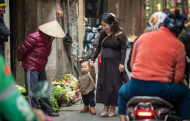 Ağır hamile Vietnamlı bir kadın, genç oğlunun elini tutuyor ve bir tüccar gibi gülümsüyor. Meşgul Kham Thien Pazarı Sokağı 'nda. Hanoi, Vietnam' daki çocuğa güzel bir şey söylüyor..