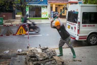 A worker smashes concrete with a sledgehammer on the pavement in Danang, Vietnam. clipart