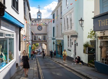 İnsanlar 14. yüzyılın doğu kapısı kemerinin yanında yürüyorlar. Büyük saati Totnes, Devon, İngiltere 'deki ana caddenin üzerinde duruyor..