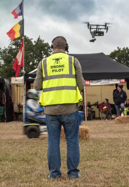 Önlük giyen profesyonel bir İHA pilotu, Billingshurs, West Sussex, İngiltere 'deki bir çim biçme makinesi yarışı toplantısını kaydederken İHA uçuruyor..