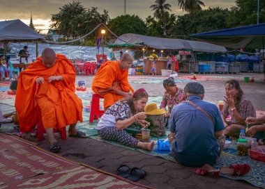Kamboçyalı bir grup insan Phnom Penh, Kamboçya 'daki gece pazarında yemek yemek için yerde otururken, iki Buda' lı keşiş izliyor..