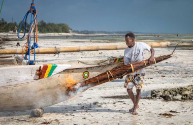 Bir adam geleneksel ahşap tekne Jambiani, Zanzibar, Tanzanya 'yı yakmak ve su geçirmez kılmak için yanan palmiye yapraklarını kullanır.