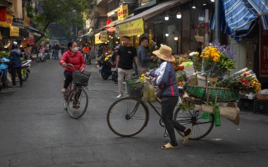 Bir çiçekçi, yüklü bisikletini başka bir bisikletçinin yanından geçirir. Cau Go 'da, Hanoi, Vietnam' daki Eski Bölge 'de bir dükkan..