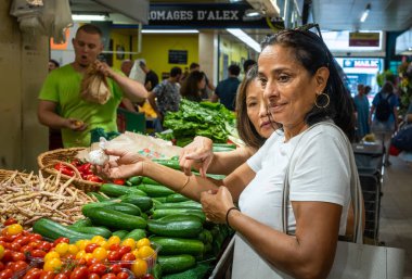 Women buy garlic and other vegetables at a stall at the indoor Montrouge Sunday market in the suburbs of Paris, France. clipart