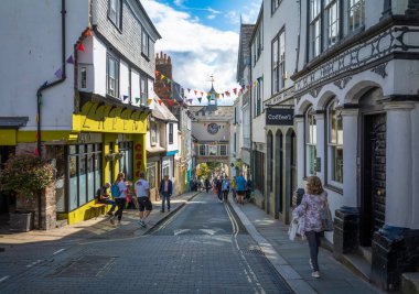 İnsanlar 14. yüzyılın doğu kapısı kemerinin yanında yürüyorlar. Büyük saati Totnes, Devon, İngiltere 'deki ana caddenin üzerinde duruyor..