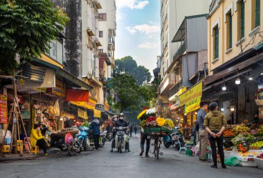 Bir çiçekçi yüklü bisikletini Hanoi, Vietnam 'daki eski bir semtte, Cau Go' daki işlek dükkanların önünden geçiriyor..