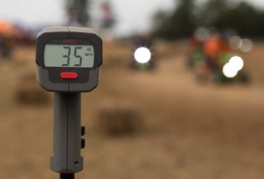 Dijital ekran göstergeli bir elektronik hız silahı saatte 35 mil hızla giden çim biçme makinelerini yarıştırır (56 km / s))
