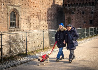 Yaşlı bir İtalyan çift Fransız Bulldog 'larıyla birlikte Milano, Lombardy, İtalya' da Castello Sforzesco ya da Milan Castle duvarlarının yanında yürür..